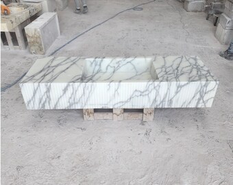 May include: A white marble bathroom sink with a rectangular basin and a textured surface. The sink is sitting on a wooden pallet.