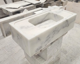 May include: A white marble sink with a rectangular shape and a single basin. The sink is sitting on a white marble pedestal.