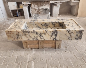 May include: A large, rectangular, white marble sink with a brown wooden base. The sink has a white and brown marbled pattern.