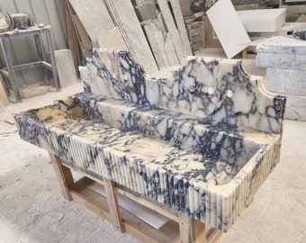 May include: A double sink vanity made of white and black marble with a decorative backsplash. The sink has a rippled edge and is mounted on a wooden frame.