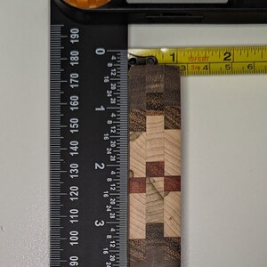 May include: A close-up of a wooden chopping board with a checkered pattern in shades of brown, beige, and red. The board is measured with a ruler and tape measure, showing it is approximately 3.8 cm wide.