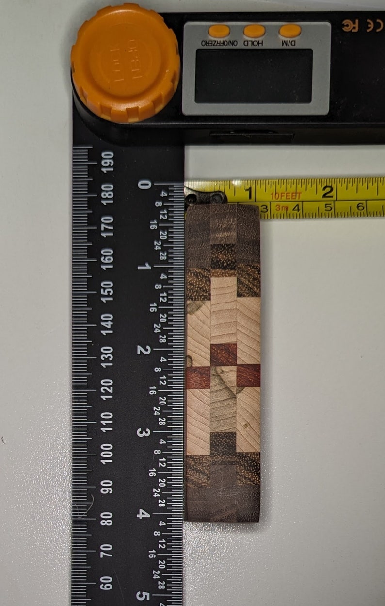 May include: A close-up of a wooden chopping board with a checkered pattern in shades of brown, beige, and red. The board is measured with a ruler and tape measure, showing it is approximately 3.8 cm wide.