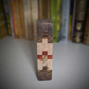 May include: A wooden block with a geometric pattern of different coloured woods. The block is made of light brown, dark brown, and red wood.