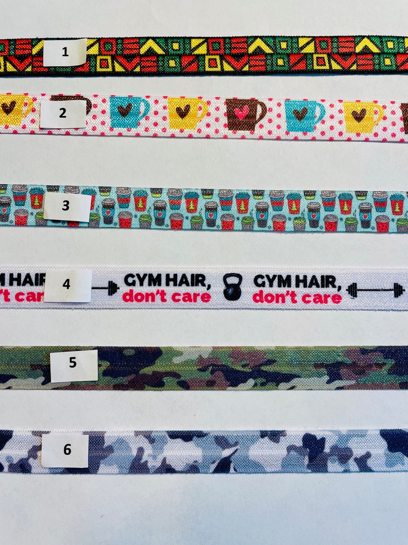 May include: Six different patterned hair ties, numbered 1 through 6. The hair ties are all about 1 inch wide and have different patterns, including geometric, coffee cups, and camouflage.