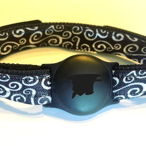 May include: Black and white patterned wristband with a black round tracker attached. The tracker has a black silhouette of a person on it.