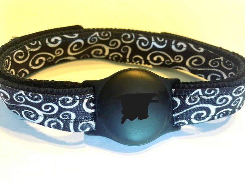May include: Black and white patterned wristband with a black round tracker attached. The tracker has a black silhouette of a person on it.