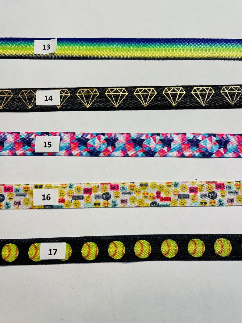 May include: Five different types of elastic hair ties with various patterns. The hair ties are numbered 13 through 17. The patterns include a gradient of blue to green, a black background with gold diamond shapes, a pink and blue geometric pattern, a white background with yellow smiley faces and text, and a black background with yellow softball shapes.