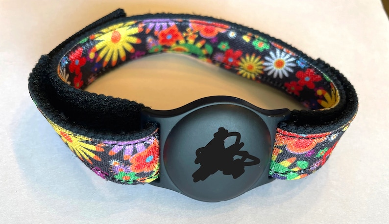 May include: A black and colorful floral patterned wristband with a black round tracker attached.