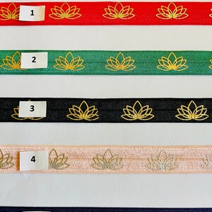 May include: Five different elastic hair ties with a lotus flower design. The hair ties are red, green, black, pink, and purple. The lotus flowers are gold on the red, green, black, and pink hair ties. The lotus flowers on the purple hair tie are a multi-colored paisley design.