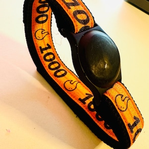 May include: Orange and black wristband with the text "1000 1000" and a small black light.