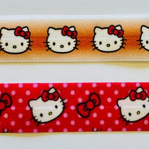 May include: Two strips of elastic ribbon featuring Hello Kitty character graphics. The top strip has an orange gradient background with repeating white cat faces and red bows. The bottom strip is red with white polka dots and Hello Kitty faces.
