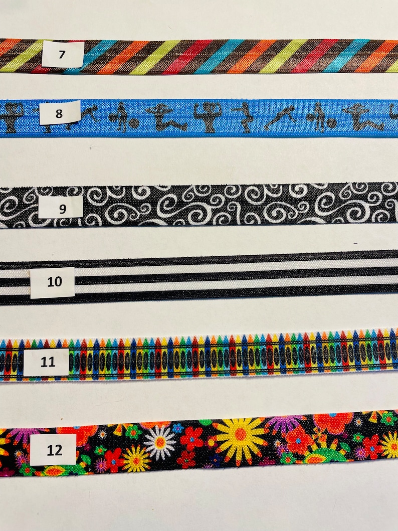 May include: Six different colorful fabric ribbon trims with numbers 7 through 12 printed on white labels. The trims feature various patterns including stripes, swirls, crayons, and flowers.