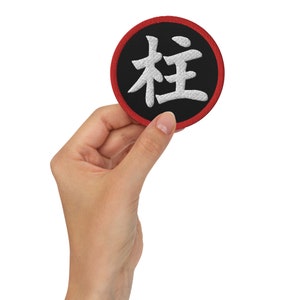 Peut inclure: Un patch circulaire noir et rouge avec des caractères kanji brodés en blanc. Les caractères kanji sont "Arbre" et "Vie".