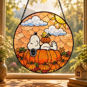 May include: A circular stained glass suncatcher featuring a white beagle lying on a large orange pumpkin in a field of pumpkins and autumn leaves. A small yellow bird sits on a smaller pumpkin atop the beagle, with white clouds and a yellow sun.