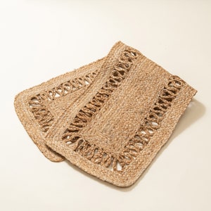 May include: Two rectangular jute placemats. The placemats are a natural tan color with a woven texture. Each placemat has a decorative border with a cut-out design. The placemats are slightly overlapping.