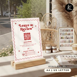 Puede incluir: Un soporte de madera que sostiene un letrero con la frase "Leave a Review" en escritura roja. El letrero incluye un código QR e información de redes sociales. Disponible en A4 y US Letter.