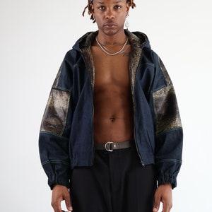 May include: A dark blue denim jacket with a hood, featuring a snakeskin pattern on the sleeves and back. The jacket has a zip fastening and a silver belt.