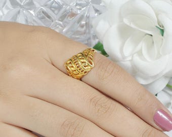 May include: A gold-colored ring with an openwork design, featuring a series of curved, interconnected elements. The ring is worn on a finger, showcasing its intricate details and bright, reflective surface. The ring's design has a leaf-like shape.
