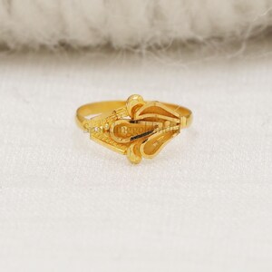 May include: A polished yellow gold ring featuring a central decorative element composed of three interconnected, teardrop-shaped loops with a smooth, reflective finish. The band is slender and plain, showcasing a bright, metallic gold lustre throughout.