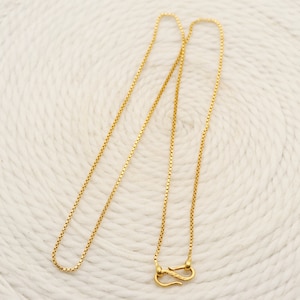 Puede incluir: Un collar de cadena de oro con cierre de caja. La cadena es fina y delicada, y el cierre es un diseño simple y seguro.