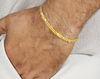 May include: A thin, yellow gold chain bracelet with a textured, repeating link pattern. The bracelet is worn around the wrist, showcasing a polished metallic finish and a consistent, interlocking design that creates a subtle, continuous visual texture.