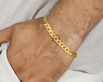 May include: A gold-toned chain bracelet featuring a series of interlocking, flat, rectangular links. The bracelet has a polished, reflective surface and is worn around the wrist, showcasing a classic, uniform design with a secure, continuous link structure.