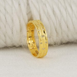 May include: A polished yellow gold ring featuring a repeating textured pattern of horizontal bars and vertical segments. The band has a smooth, rounded interior and a reflective metallic finish, showcasing a consistent design around the entire circumference.