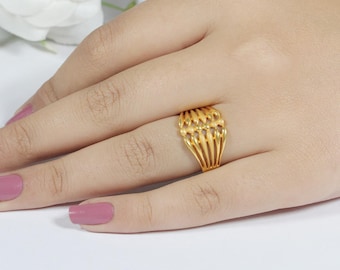 May include: A gold ring with an openwork design is displayed on a hand. The ring features a series of vertical bars connected by a decorative top section. The ring is a bright, shiny gold color.