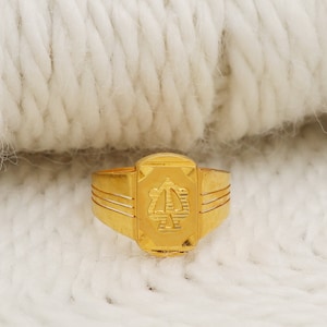 May include: A gold ring with a square design and a raised letter "A" in the center.