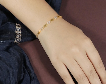 Pode incluir: Uma pulseira dourada com um design delicado. Apresenta elos ovais, alguns adornados com pequenas pedras preciosas transparentes. A pulseira é usada no pulso, mostrando seus detalhes intrincados e estilo elegante. Comprimento: aproximadamente 17 cm.