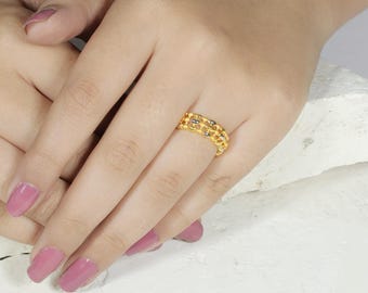 May include: A gold-colored ring with a chain-link design. The ring is worn on a finger, showcasing its intricate details and polished finish. The ring's design features a series of interconnected links, creating a textured and eye-catching appearance.