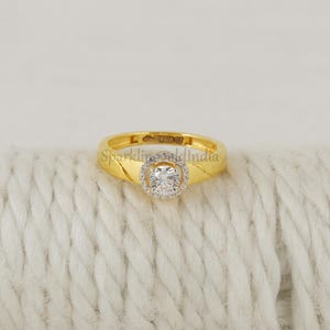 May include: A gold ring featuring a central round brilliant-cut stone surrounded by a halo of smaller stones. The band is smooth and polished gold. The interior of the band is engraved with the text SparklingGoldIndia and other markings.