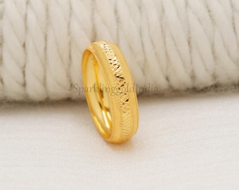 May include: A gold ring with a textured design. The ring has a band with a repeating geometric pattern and a polished finish. The ring is set against a white background.