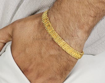 May include: A gold-toned bracelet featuring a series of rectangular, textured links connected in a continuous chain design. The metal surface displays a repeating pattern of small, raised dots and horizontal grooves across each individual link.