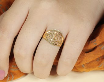 May include: A gold-colored ring with an intricate openwork design featuring a pattern of stars or floral shapes. The ring is set on a finger, showcasing its detailed craftsmanship and elegant appearance. The ring's design is highlighted against a warm, orange background.