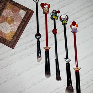 Può includere: Set di sei pennelli da trucco neri e rossi con topper a forma di personaggi di clown colorati. I pennelli hanno forme e dimensioni diverse per varie applicazioni di trucco.