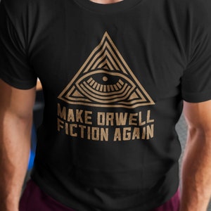 Op de afbeelding: Een zwart T-shirt met een gouden afbeelding van een oog in een driehoek. De tekst "Make Orwell Fiction Again" staat onder de afbeelding.