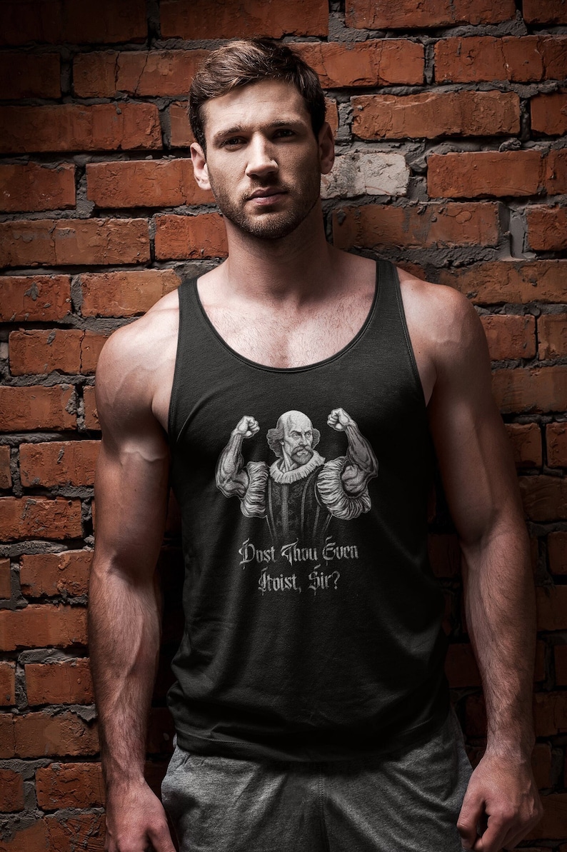 Op de afbeelding: Zwart tanktop met een afbeelding van William Shakespeare die zijn biceps spant. De tekst "Dost Thou Even Hoist, Sir?" staat onder de illustratie. De persoon staat voor een bakstenen muur.