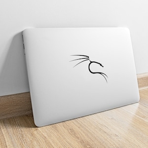 Könnte beinhalten: Ein weißer Laptop mit einem schwarzen, stilisierten Drachenlogo auf dem Deckel. Der Laptop steht auf einer hellbraunen Holzoberfläche.