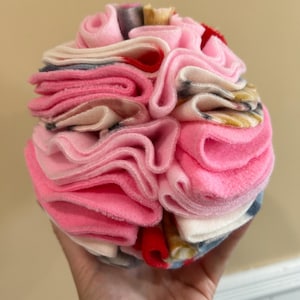 May include: A pink and white fabric ball with a ruffled texture. The ball is made of multiple layers of fabric, creating a layered and textured look.
