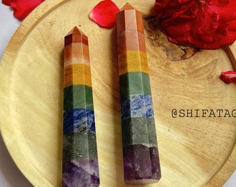 May include: Two rainbow chakra wands, each with seven different colored stones, are displayed on a wooden plate. The wands are made of amethyst, lapis lazuli, sodalite, green aventurine, citrine, carnelian, and red jasper. The plate is surrounded by rose petals.