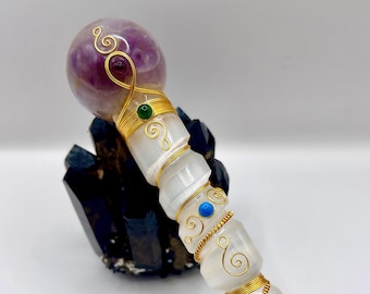 May include: A handcrafted crystal wand with a purple amethyst sphere top. The wand features clear quartz segments, gold wire accents, and colorful gemstone embellishments. The wand is approximately 20 cm long.