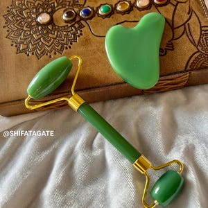 May include: A green jade roller and gua sha set. The roller has a gold handle and a green jade stone. The gua sha is heart-shaped and green.