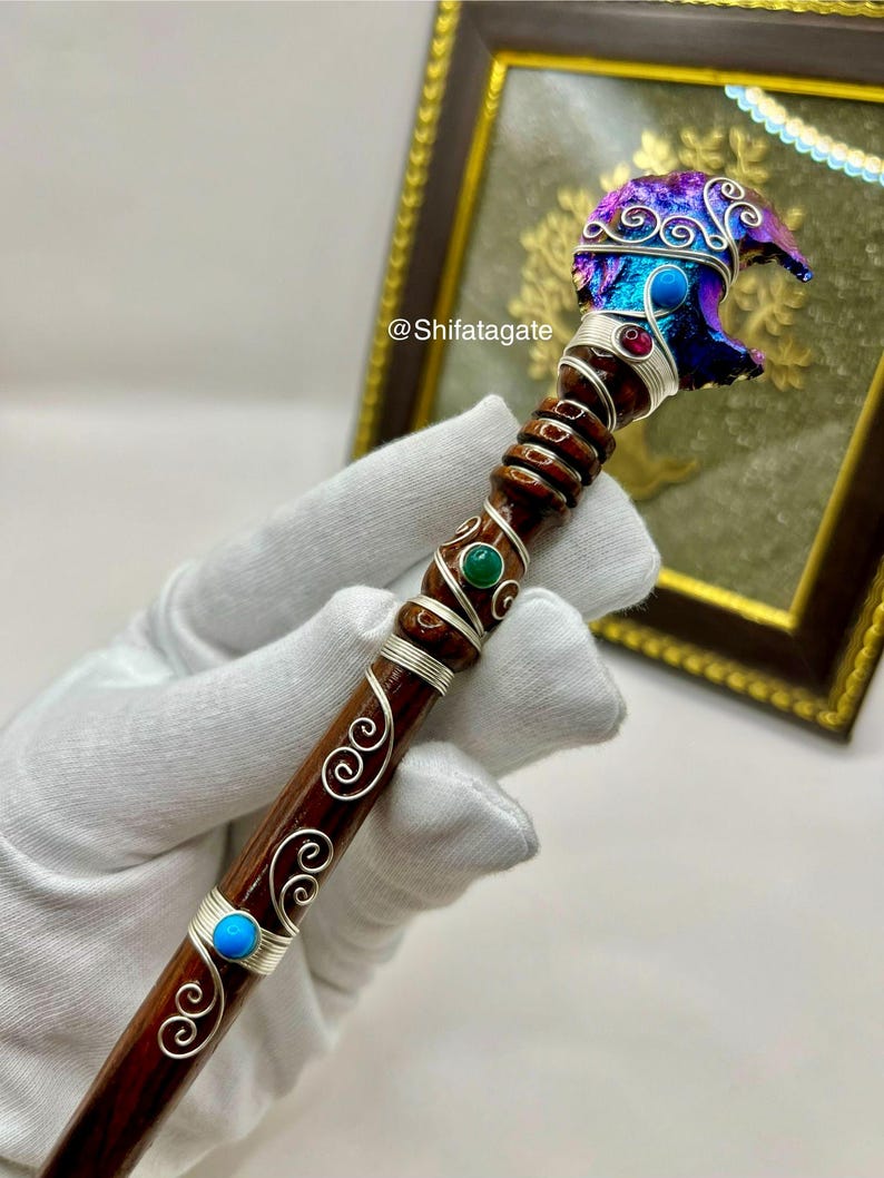 May include: A handcrafted wooden wand with a carved bear head, adorned with silver wire, colorful gemstones, and a swirling design. The bear head is a mix of blue, purple, and iridescent colors. The wand's handle is dark brown with silver wire accents.