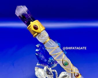 Puede incluir: Una varita de cristal con punta de amatista, detalles dorados y gemas incrustadas. La varita tiene un cuerpo cilíndrico transparente envuelto con alambre dorado y adornado con piedras rojas y verdes. El fondo es azul liso.