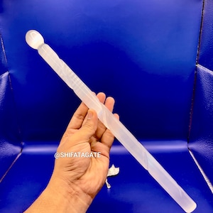 May include: A translucent, elongated wand with a rounded top and a spiraled design. The wand is held against a blue background. The product is a light, off-white color.