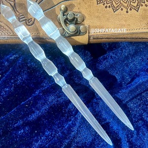 Puede incluir: Dos varitas de cuarzo transparente con una punta puntiaguda y una superficie texturizada. Las varitas están sobre una superficie de terciopelo azul.