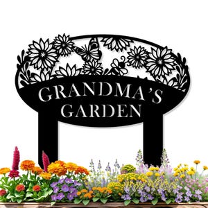May include: Black metal garden sign with the words "GRANDMA'S GARDEN" in white. The sign features a floral and butterfly design at the top. The sign is placed in a garden bed filled with colorful flowers.