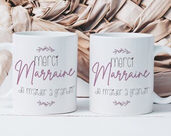 Puede incluir: Dos tazas de cerámica blanca con texto negro y un diseño floral rosa. El texto en las tazas dice "Merci Marraine de m'aider a grandir".