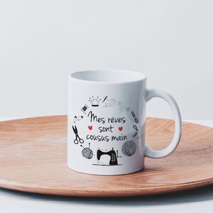 May include: White ceramic mug with a black and white illustration of sewing tools and the text "Mes r&ecirc;ves sont cousus main" with a red heart.